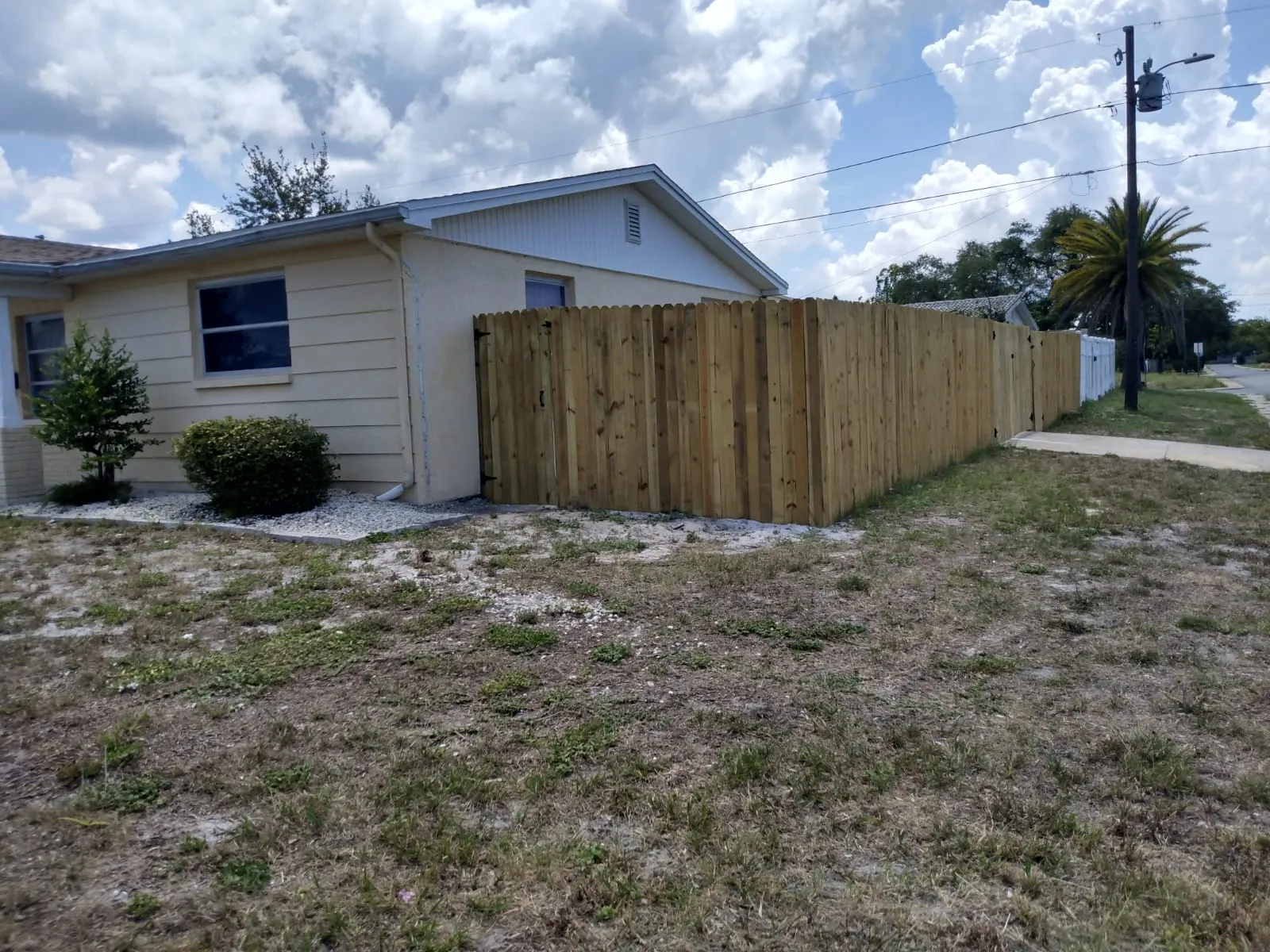 A finished wood privacy fence running along the side of a single-story house in daylight.